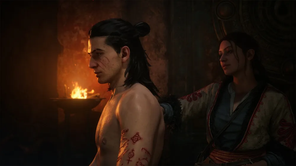 A woman tends to markings on Coen's shoulder beside a brazier in The Blood of Dawnwalker.