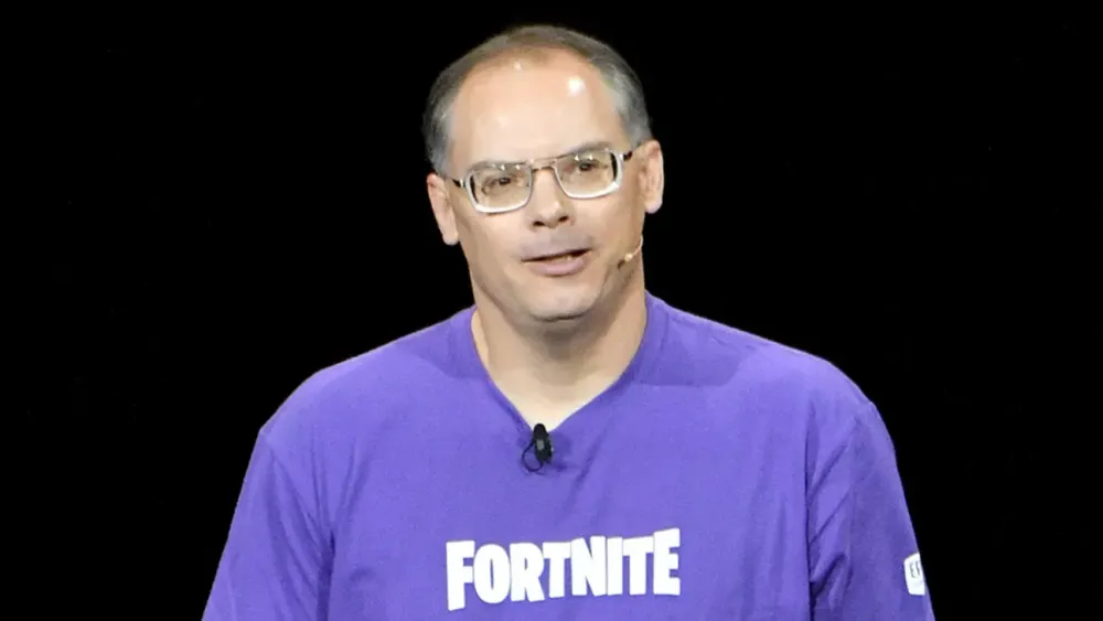 Epic Games CEO Tim Sweeney speaking on stage in a purple Fortnite T-shirt.