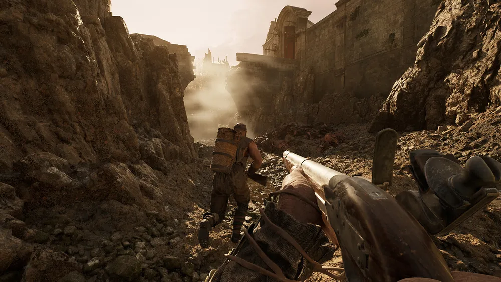 First-person view in HUNGER: a player carrying a musket follows a survivor with a wicker pack through a rocky ravine toward ruined buildings in hazy daylight.