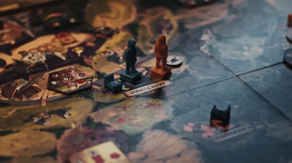 A close-up from the trailer of the assembled Kingdom Come: Deliverance board game mid-play, with the map board, tiles, and tokens laid out across a table.