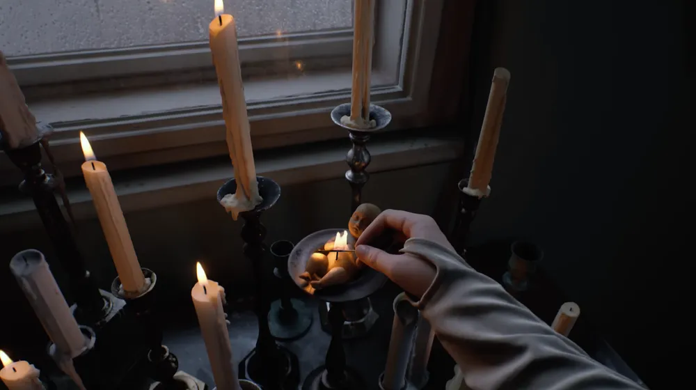 A hand reaches toward a windowsill crowded with lit candles in ornate holders next to small figurines on a metal plate, from an OD teaser.