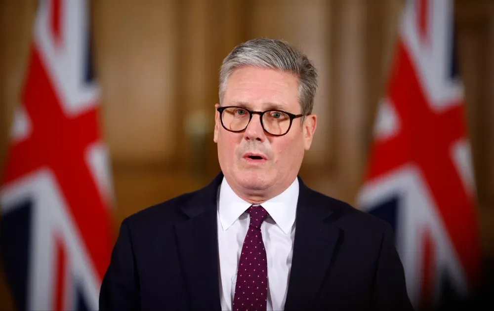 UK Prime Minister Keir Starmer speaking in front of two Union Jack flags.